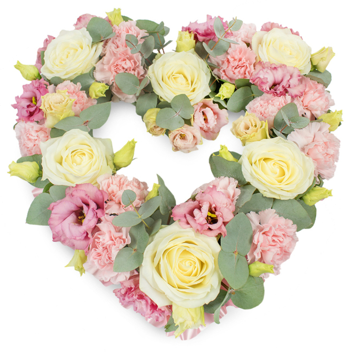 A graceful heart-shaped wreath of funeral flowers is set against a bright white background, its pastel colours and flowing textures capturing the quiet, reflective mood often felt at services around Dartford. The heart itself is fully filled with blooms, producing a lush, generous appearance with no bare spaces. Creamy white and pale yellow roses take pride of place, spaced evenly throughout the heart to create a gentle rhythm. Their velvety petals curl outward from tightly furled centres, forming elegant cup-shaped blooms that catch subtle highlights and shadows. Surrounding and softening these focal roses are clusters of delicate pastel pink carnations, their many ruffled petals overlapping in soft waves that bring a sense of movement and tender fullness. Interspersed with the carnations and roses are mauve-pink lisianthus flowers, their slightly open, bell-like petals and occasional deeper centres providing contrast and a touch of refined drama, like the changing light along the River Darent. Cool, silvery-green eucalyptus runs through the arrangement, the rounded leaves resting lightly among the petals and tracing the outline of the heart with calm, muted tones. Tiny yellow-green buds dot the design here and there, suggesting freshness and newly opened life. The whole wreath appears freshly arranged, as though just prepared by Flowers Dartford for delivery to a local church, crematorium, or home. The overall impression is of a softly spoken yet deeply felt tribute, ideal for funerals, memorial services, or anniversary remembrances, where its heart shape can quietly express love, sympathy, and the lasting bond with someone dearly missed.